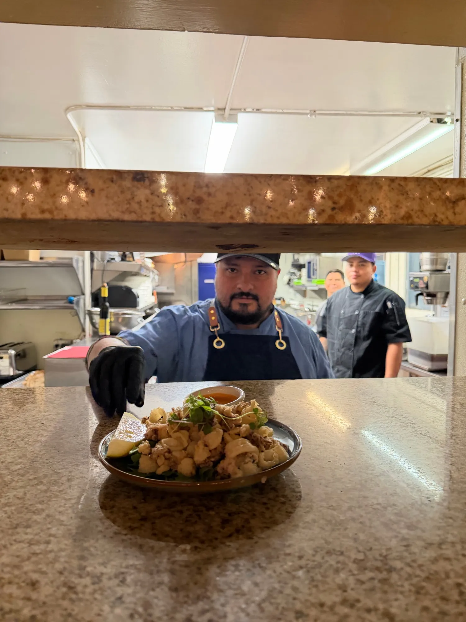 Executive Chef Hiram Diaz passing a plate of crispy calamari through the kitchen window