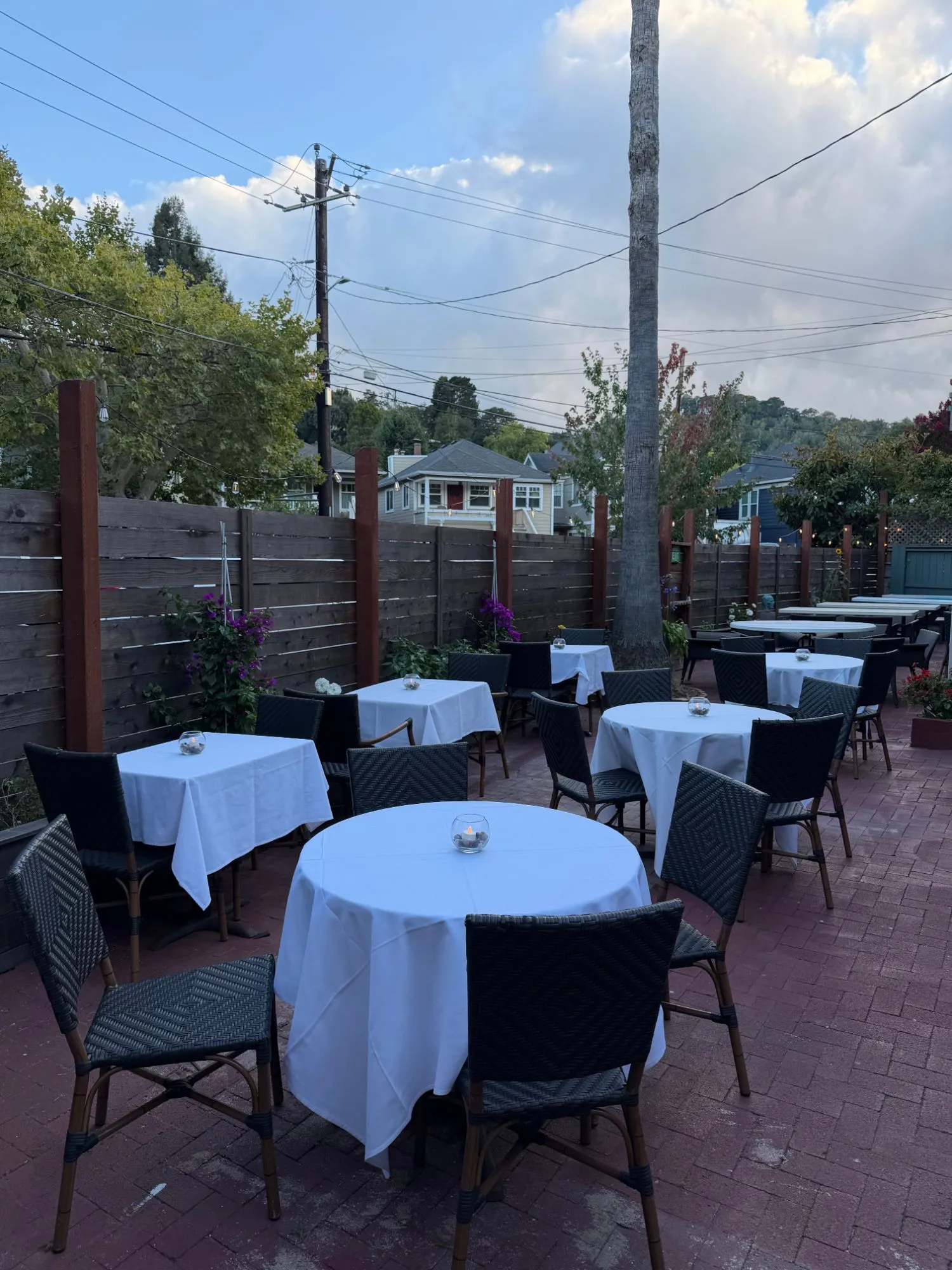 Tables laid with white cloths and candles on the garden patio at dusk